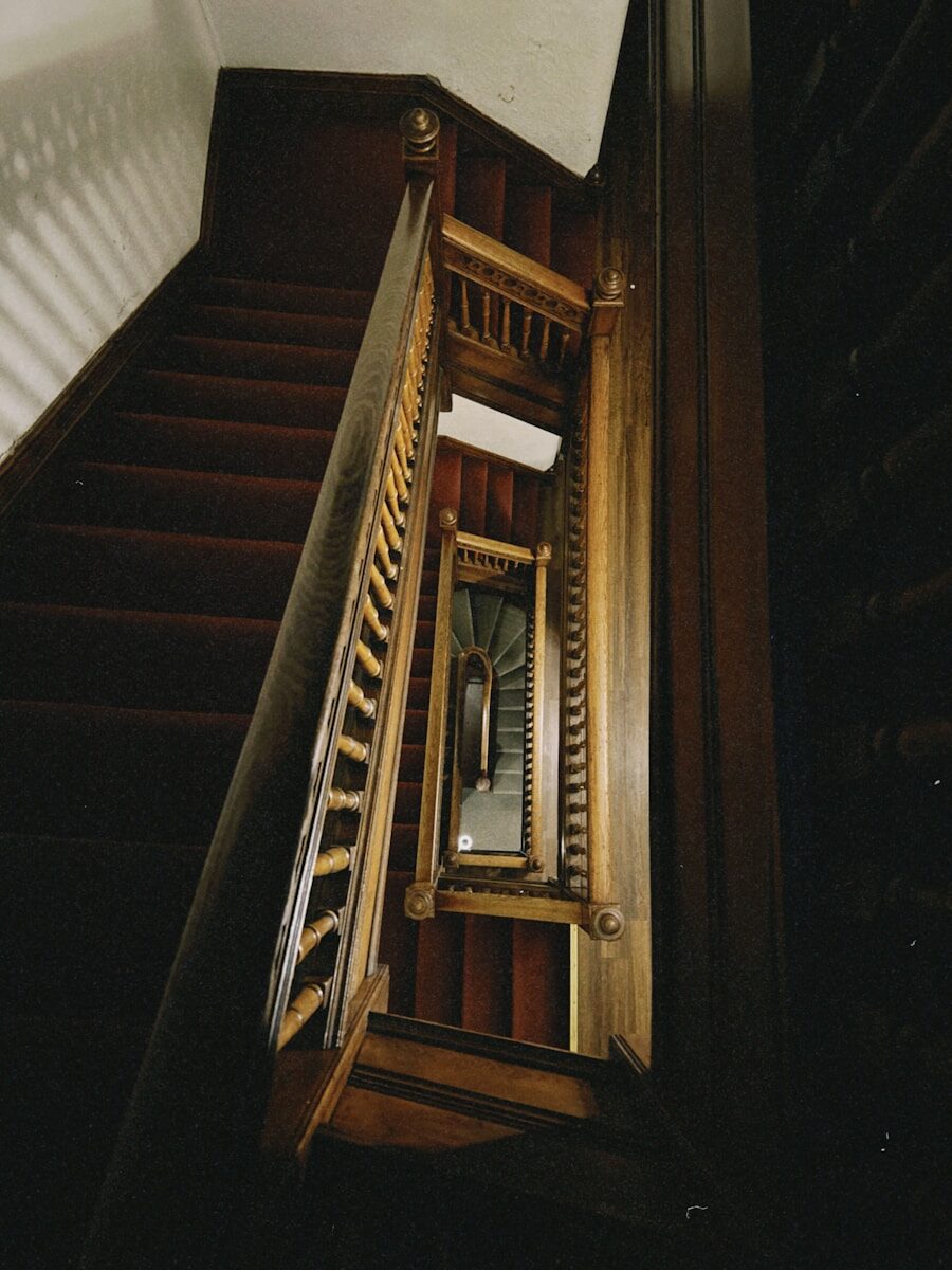 Looking down a dark wooden staircase with red carpet.